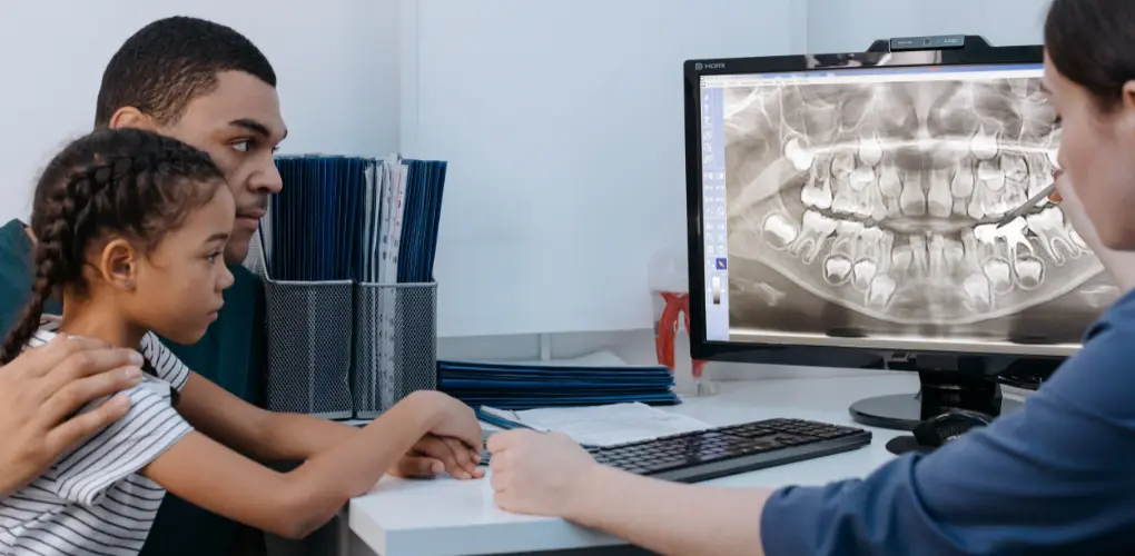 Father and young daughter reviewing an X-ray on a monitor with a dental professional